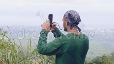 旅行男子拍摄全景照片到手机站在山顶。 游客在智能手机上拍摄视频